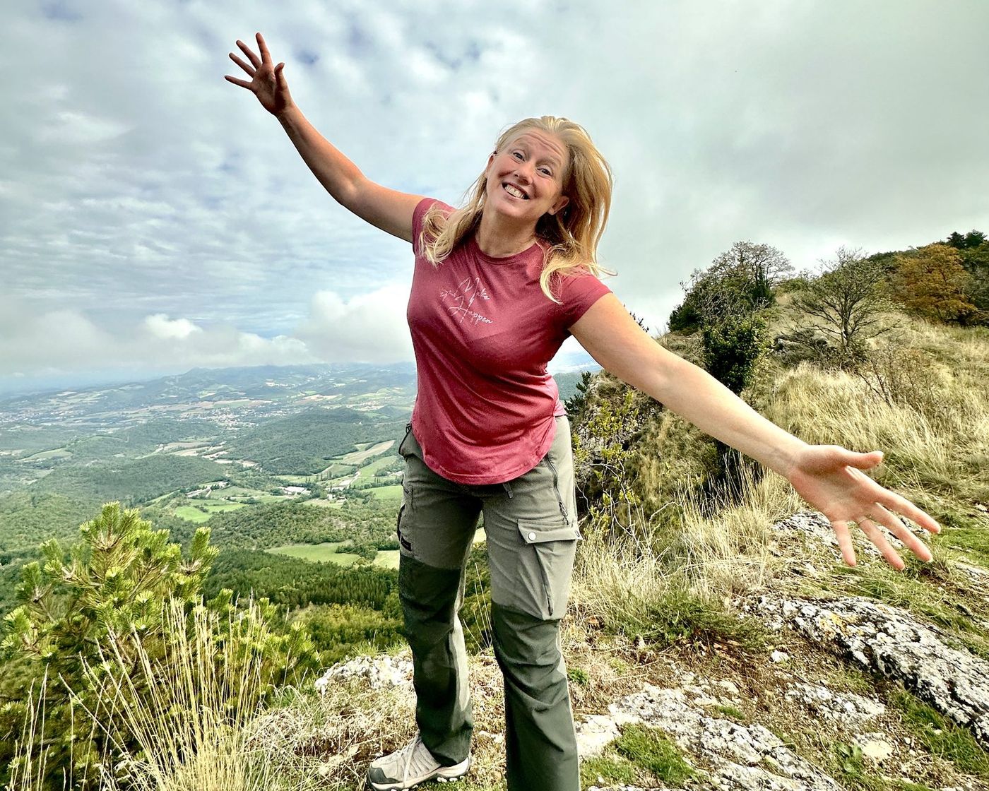 Eulalie Motte, bras grands ouverts, au sommet d'une crête, la vallée en contrebas