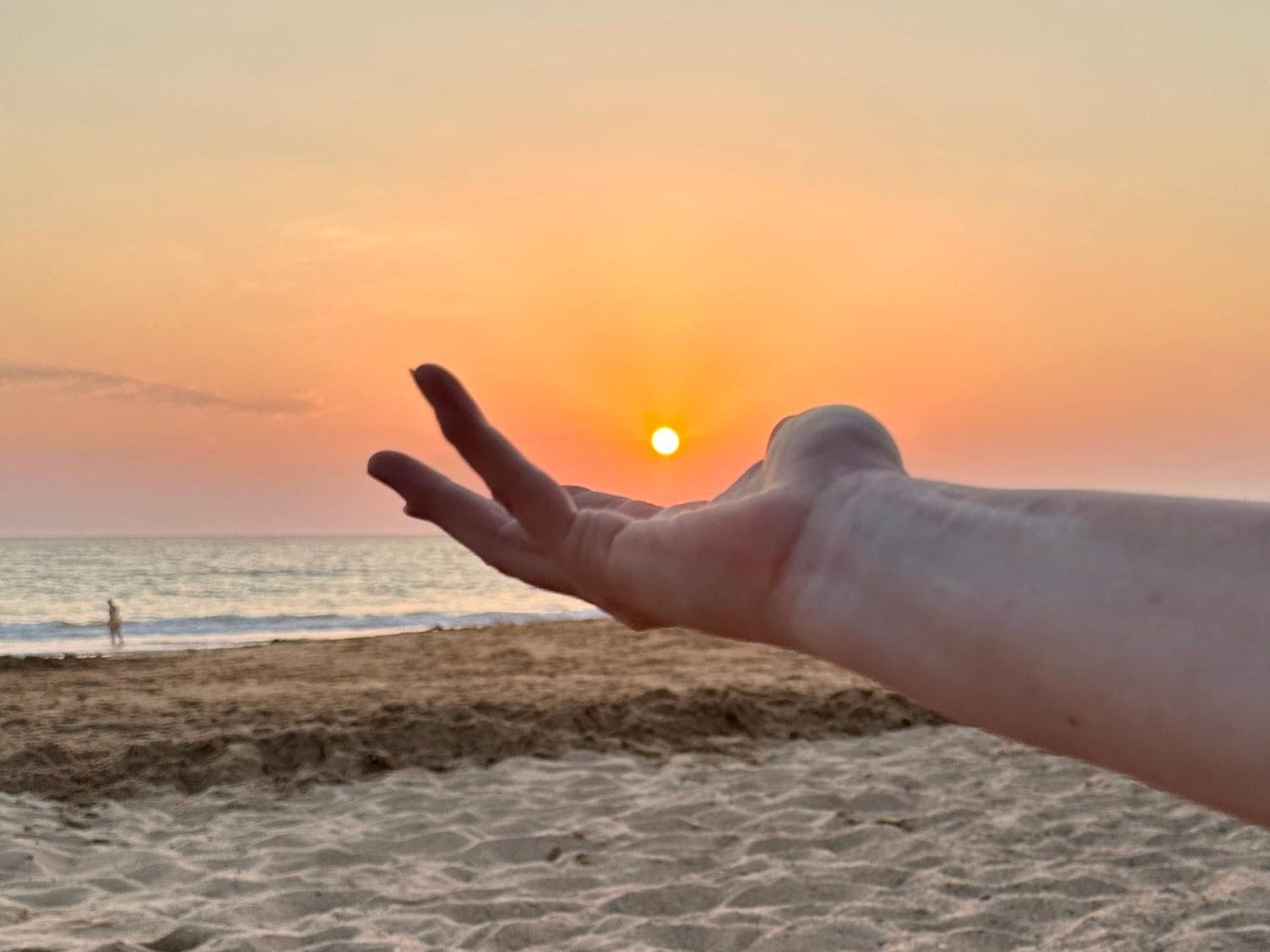 Une main ouverte qui semble porter le soleil couchant, au bord de la mer